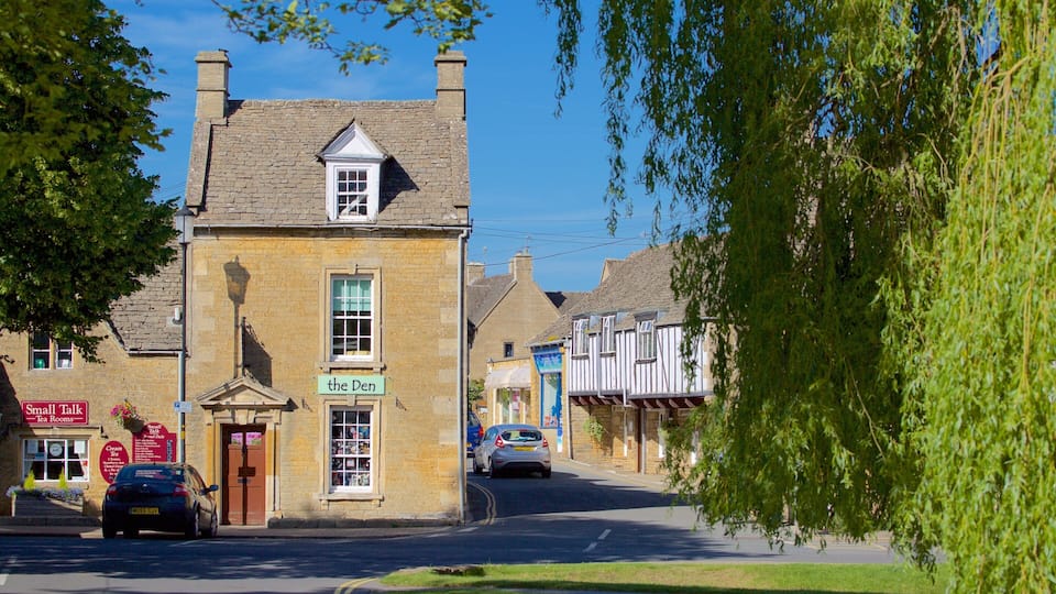 A quaint town street with a stone building labeled "the Den" and a car parked in front.