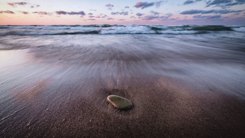 A beach with waves and a surfboard on the sand.