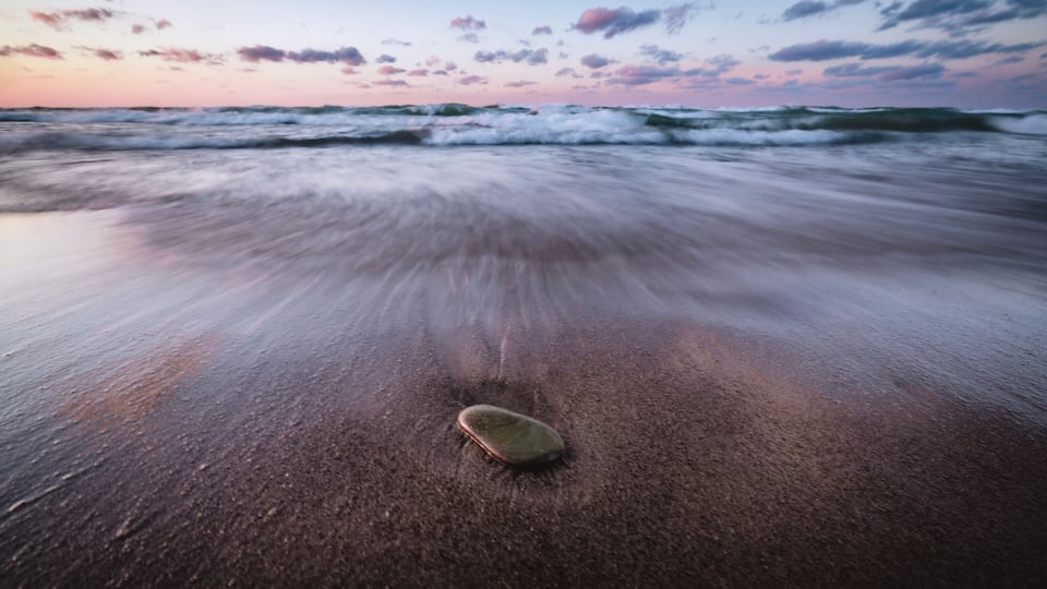 A beach with waves and a surfboard on the sand.