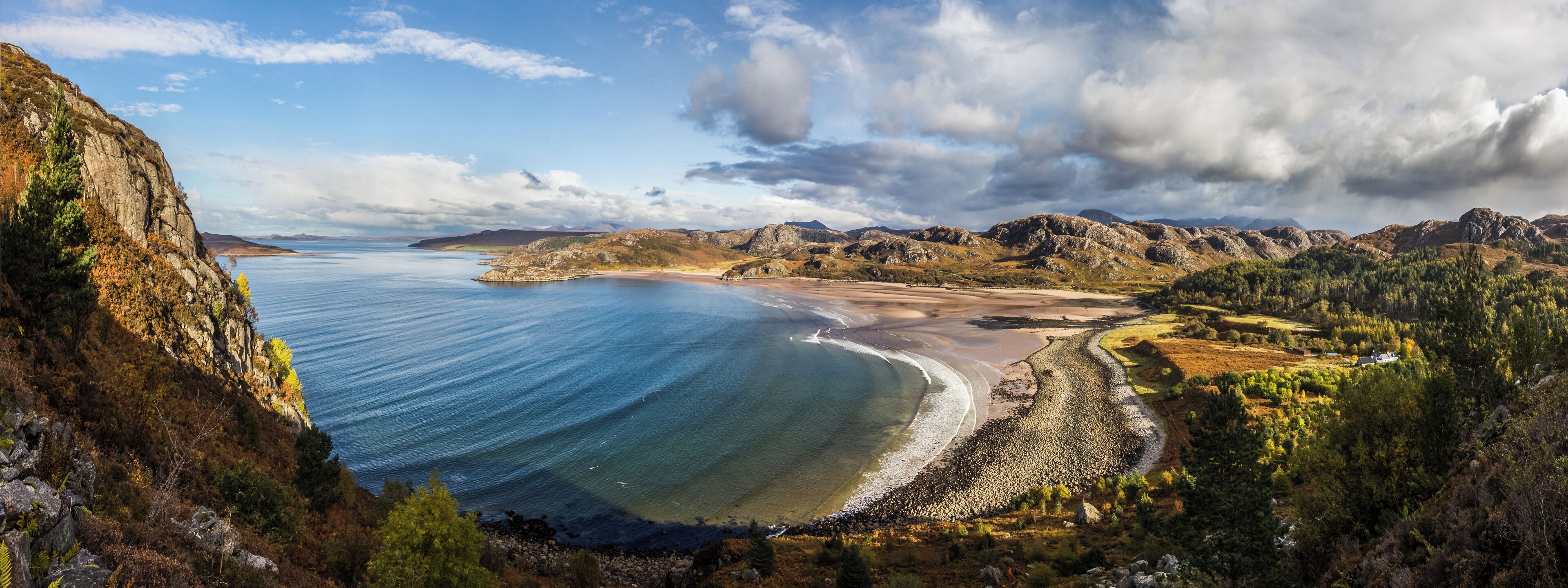 Panorama looking North down onto the beach at Gruinard Bay at roughly half tide. Gruinard Island can be seen behind the rocks in the foreground on the left. The Summer Isles can be seen behind Gruinard Island and the village of Achiltibuie is just visible in the background across the sea.