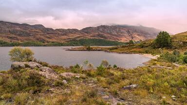 A lake surrounded by mountains and sparse vegetation.