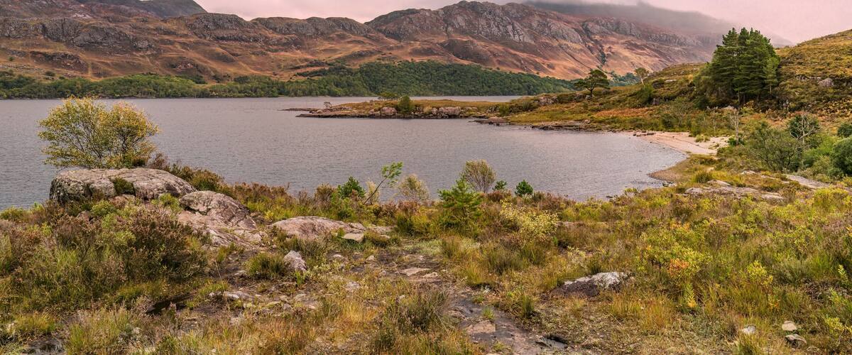 A lake surrounded by mountains and sparse vegetation.