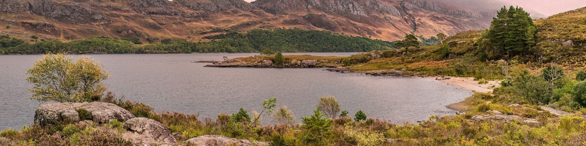 A lake surrounded by mountains and sparse vegetation.
