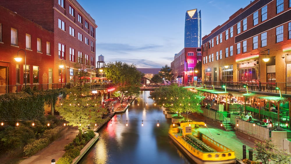 A riverside urban area with buildings, a boat, and string lights.