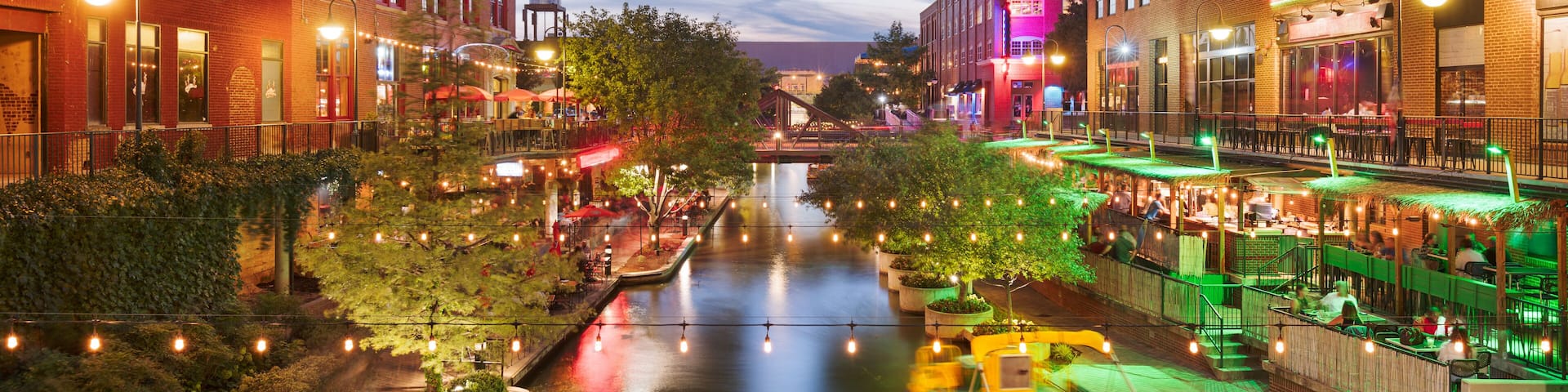 A riverside urban area with buildings, a boat, and string lights.