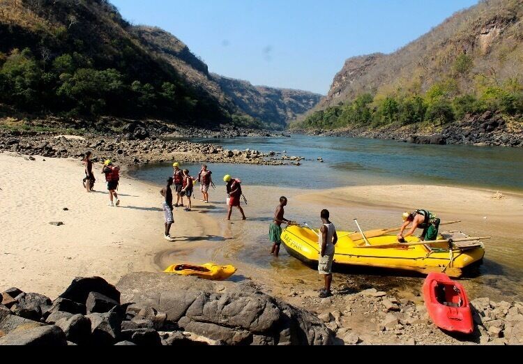 A group of people on a riverbank with boats and a rocky shoreline.