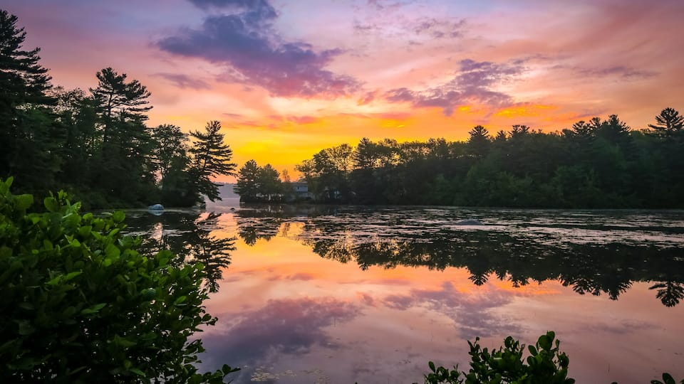 A calm river reflecting a colorful sunset sky, surrounded by dense forest.