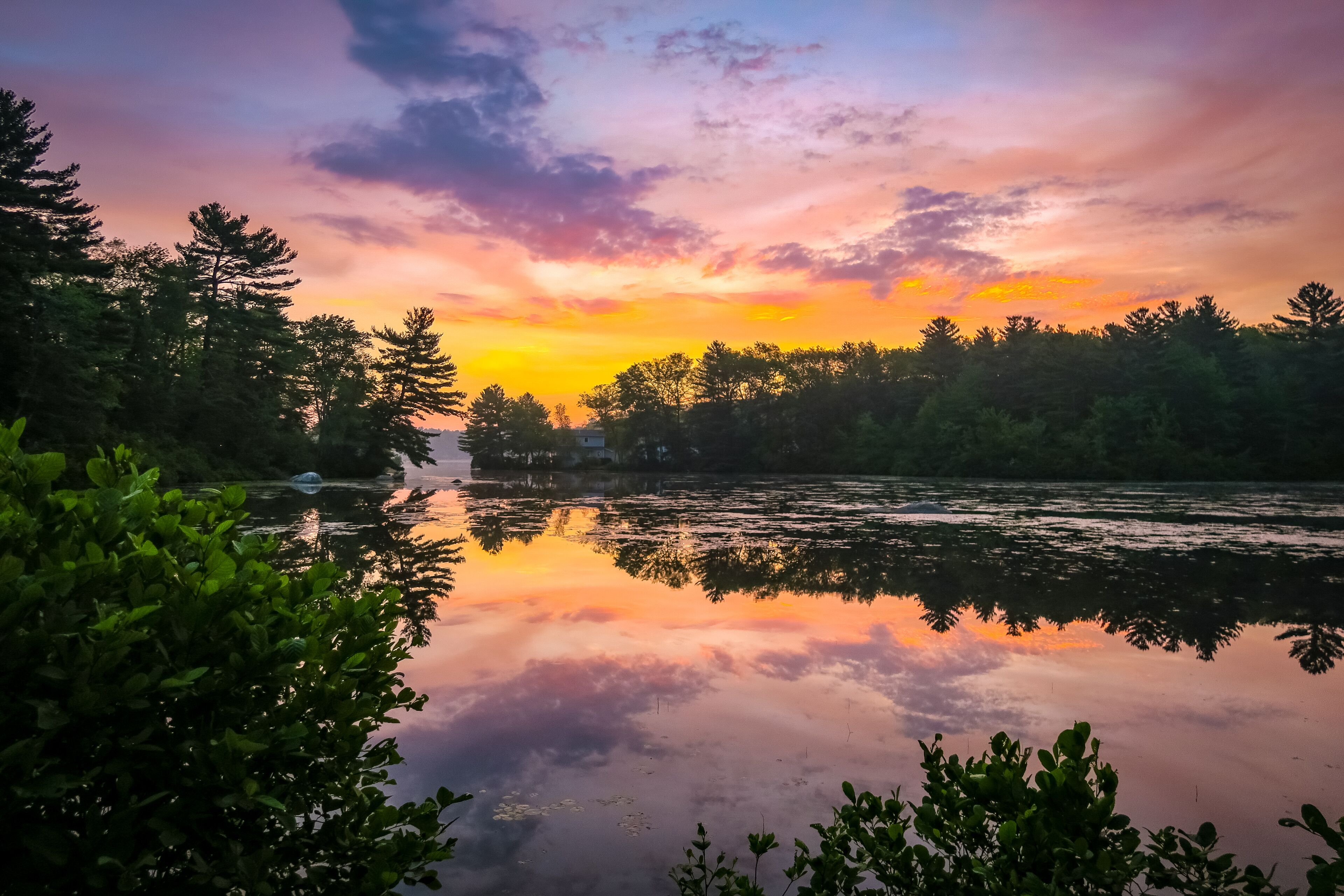 A calm river reflecting a colorful sunset sky, surrounded by dense forest.