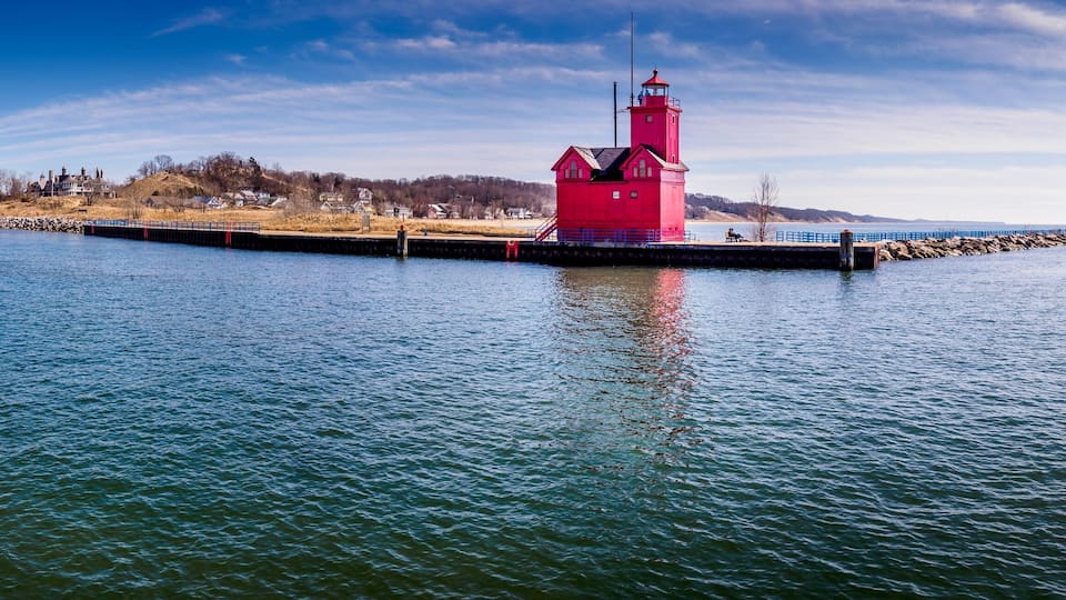 A red lighthouse on a pier with calm water and a clear sky.