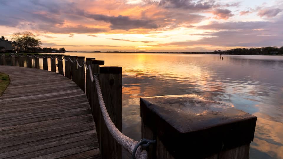 A wooden pier extending into a calm lake at sunset with a sunset in the background.