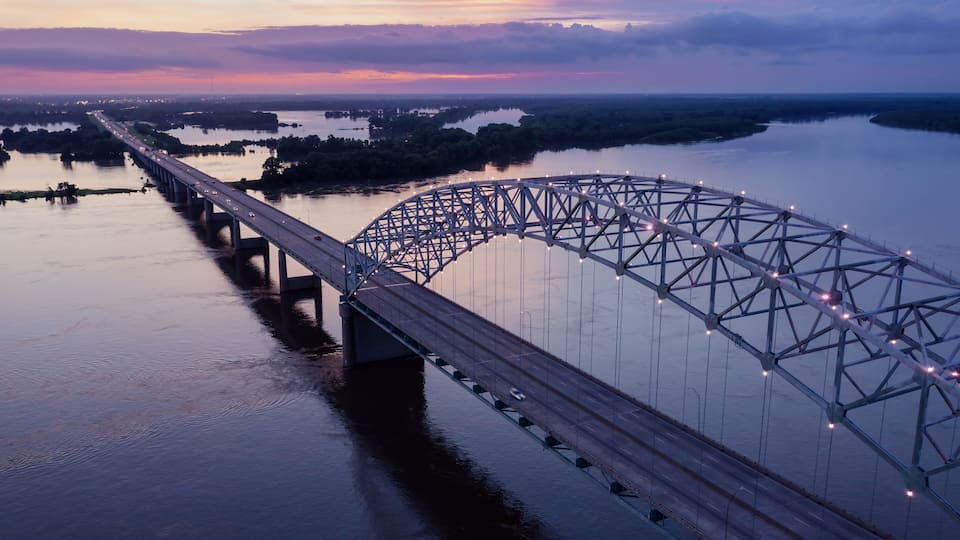 A large steel bridge spanning a wide river at dusk.