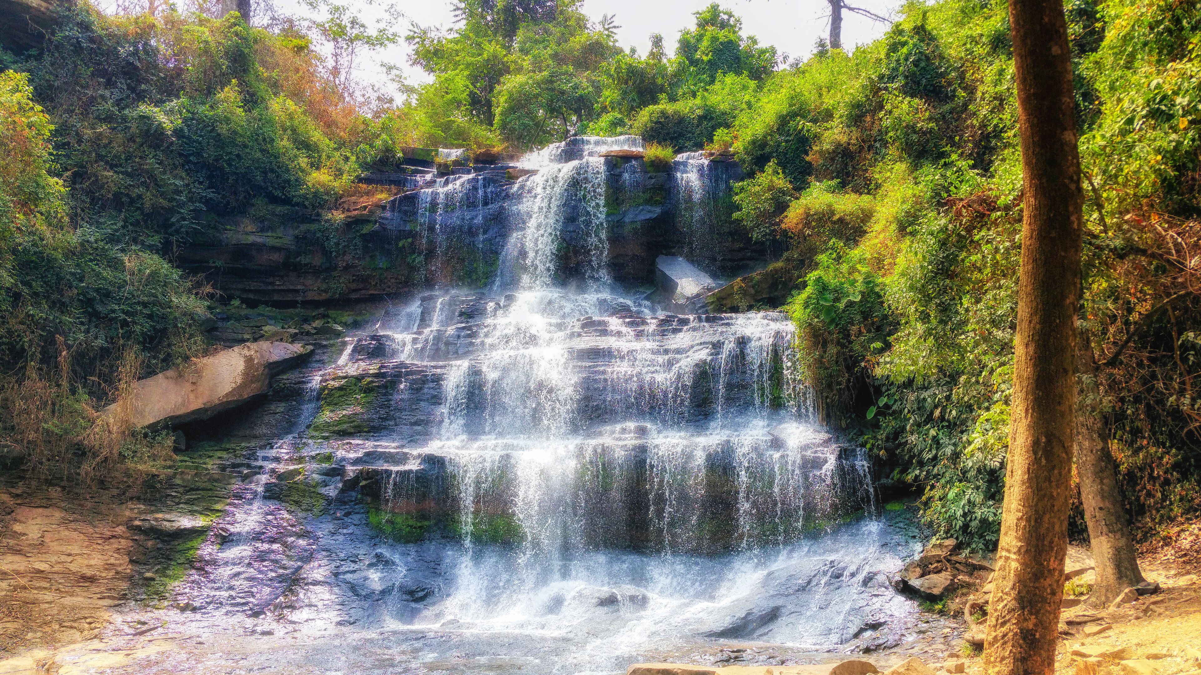 A multi-tiered waterfall surrounded by lush greenery.