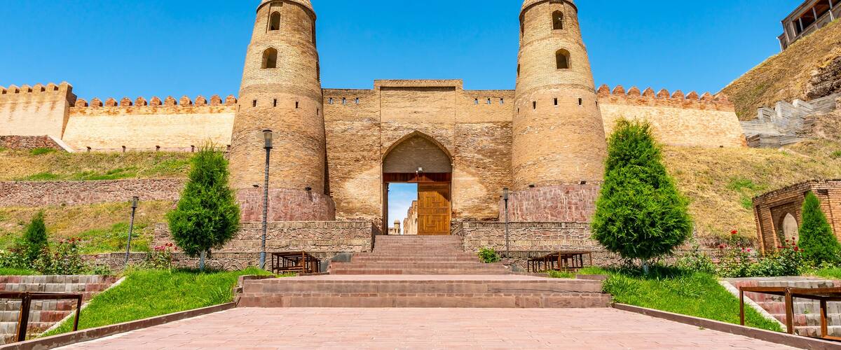 A historic stone fortress with two prominent towers, a central archway, and a paved approach leading to the entrance.