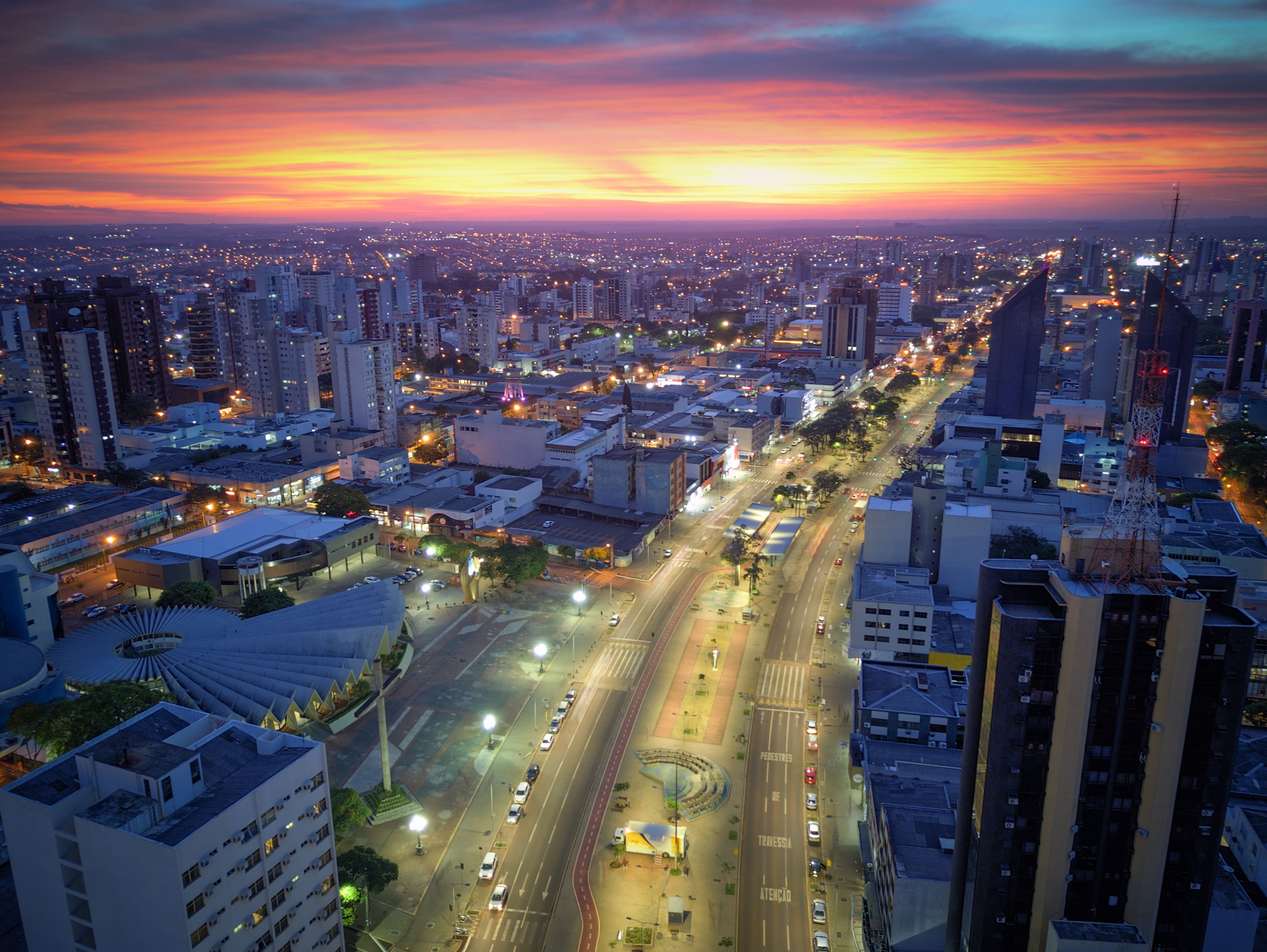 A cityscape at dusk with a sunset over a densely populated area with high-rise buildings and a busy road.