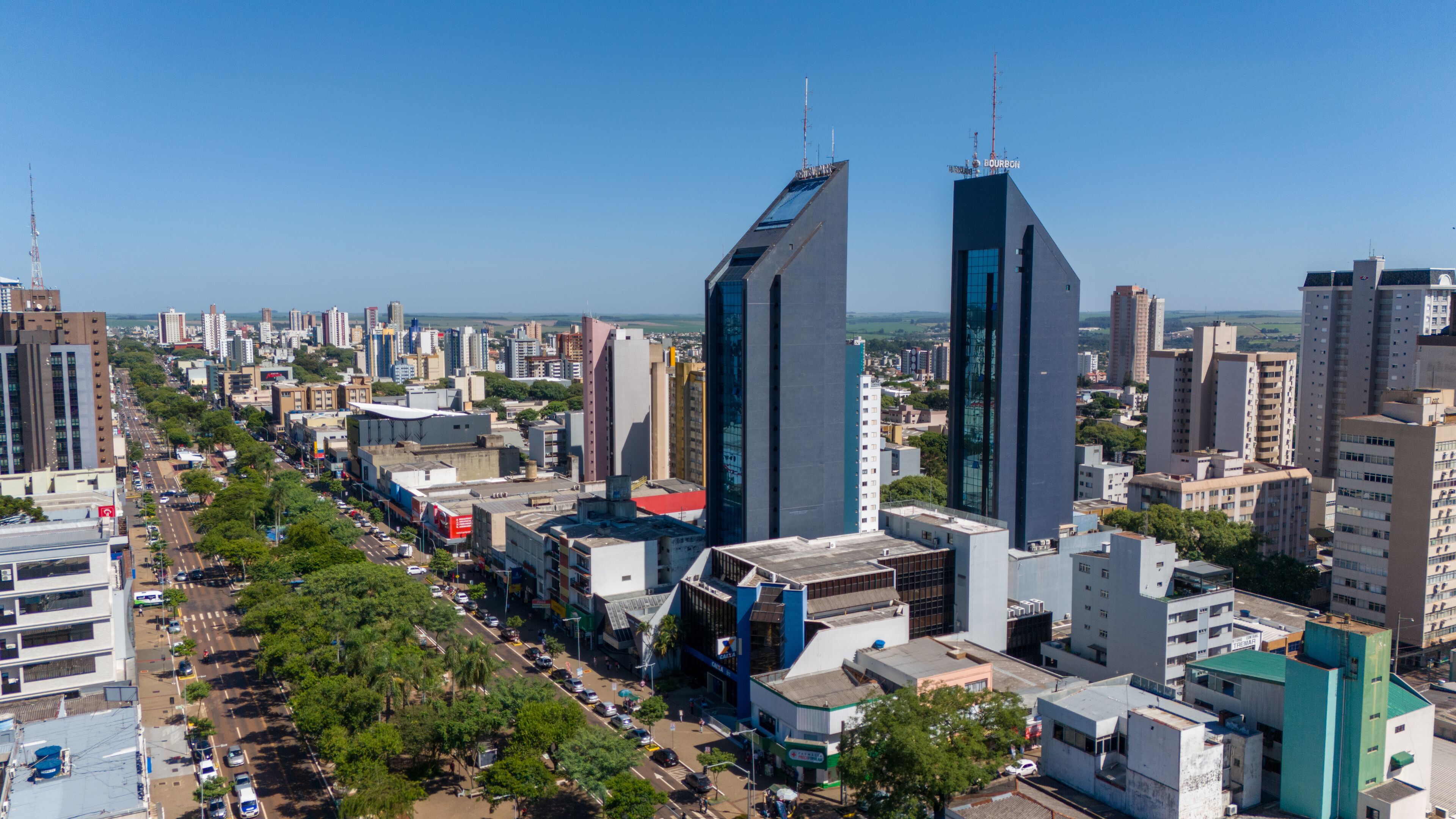 A cityscape with modern skyscrapers, a busy street lined with trees, and a clear blue sky.