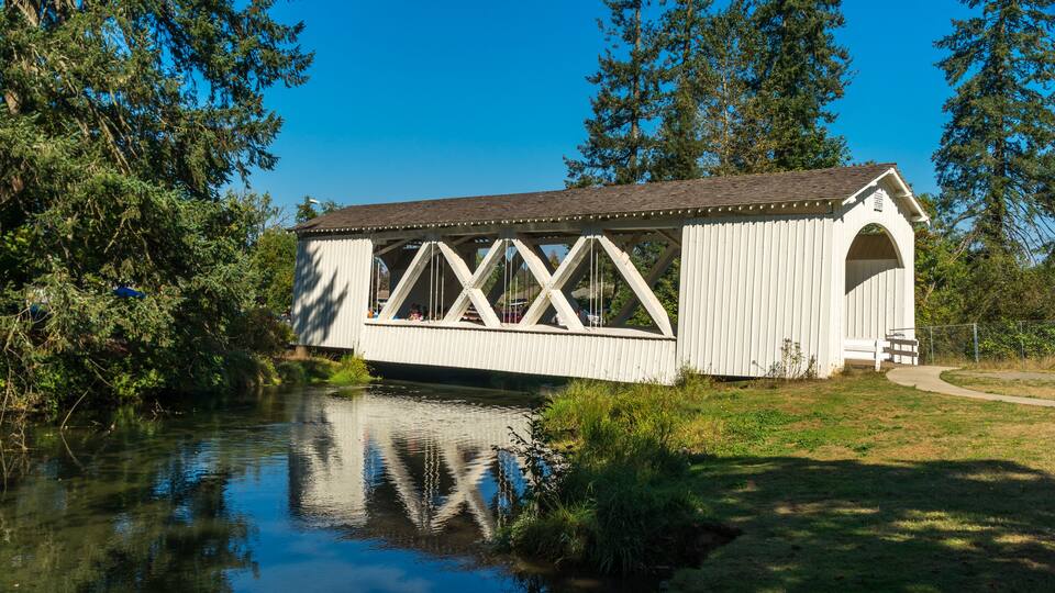 A covered bridge over a calm river, surrounded by lush greenery and trees.