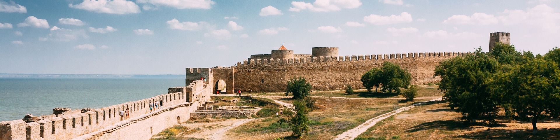 Une fortification historique offrant une vue dégagée sur la mer, dotée d’un rempart et d’un chemin menant à l’entrée.