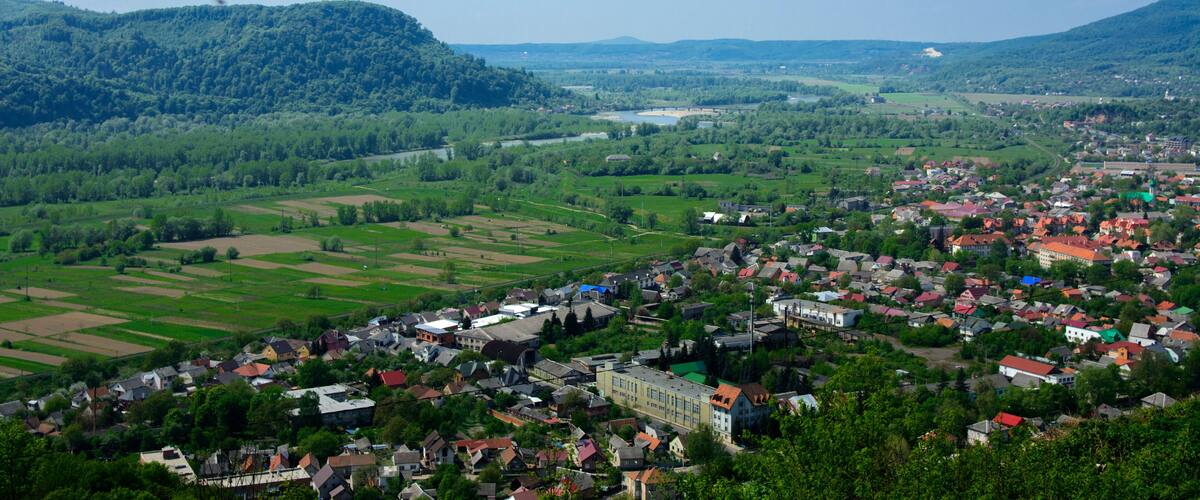 Colorful exalted view from a bird's eye view to houses in residential district in the city of Khust, Western Ukraine with high mountains in the background on a background of green vegetation.