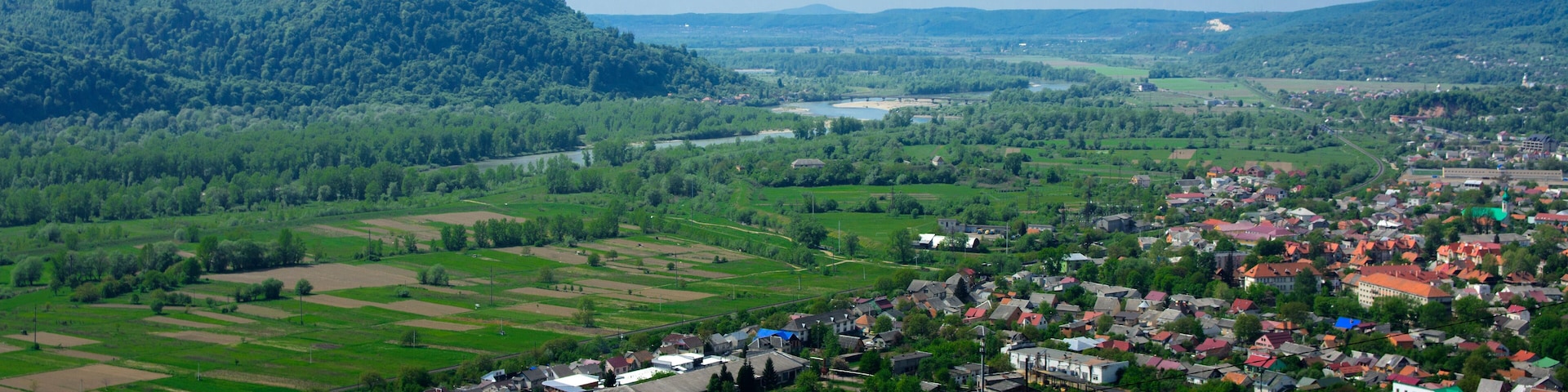 Colorful exalted view from a bird's eye view to houses in residential district in the city of Khust, Western Ukraine with high mountains in the background on a background of green vegetation.