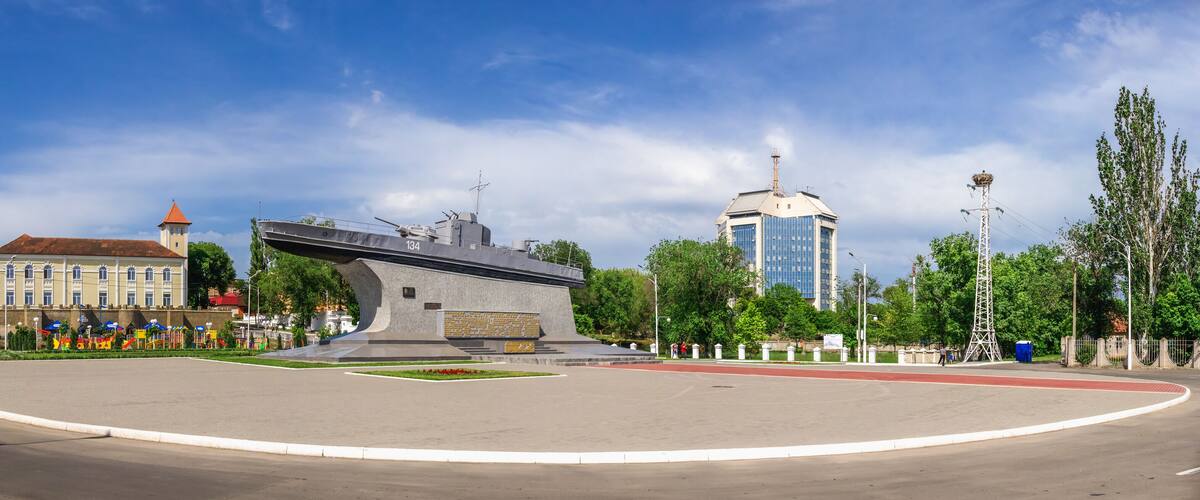 Una glorieta con un monumento, un edificio de techo rojo y un rascacielos moderno.