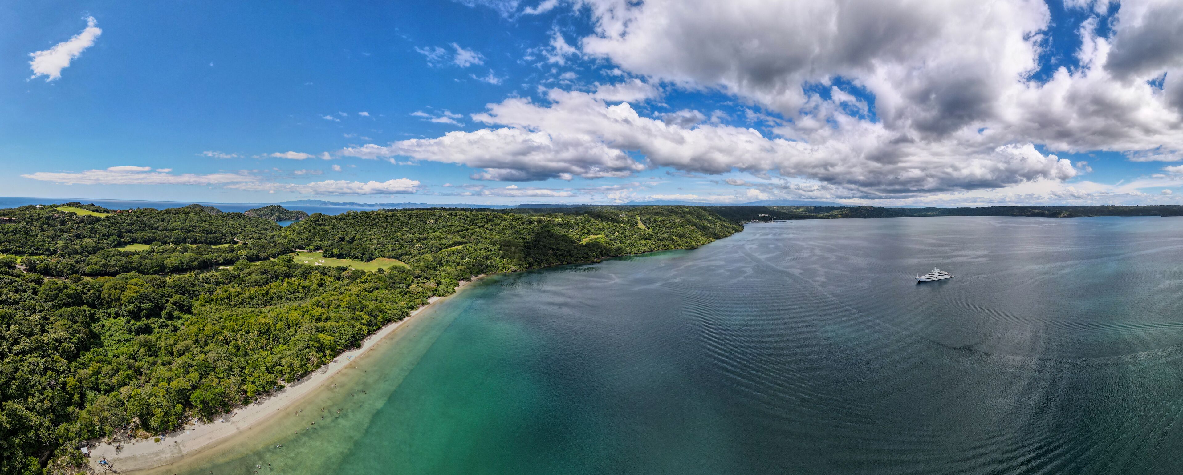 A coastal landscape with a beach, dense forest, and a calm sea with a boat.