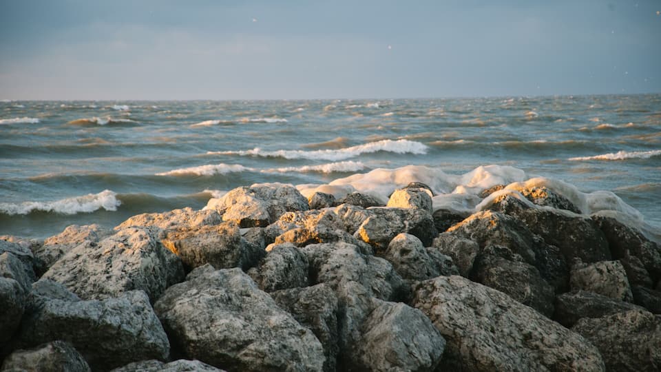 A rocky shoreline with waves crashing against the rocks under a clear sky.