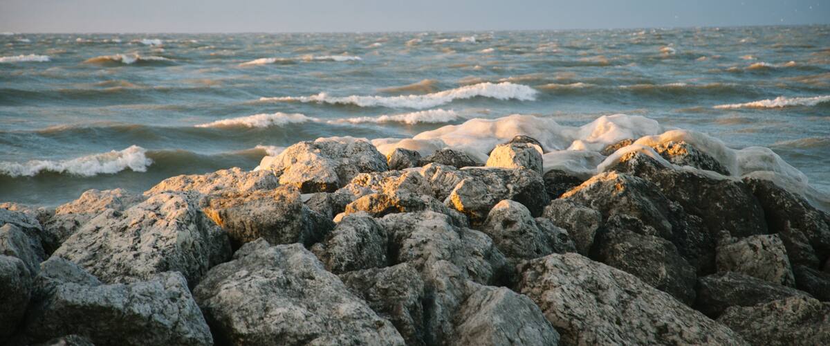 A rocky shoreline with waves crashing against the rocks under a clear sky.