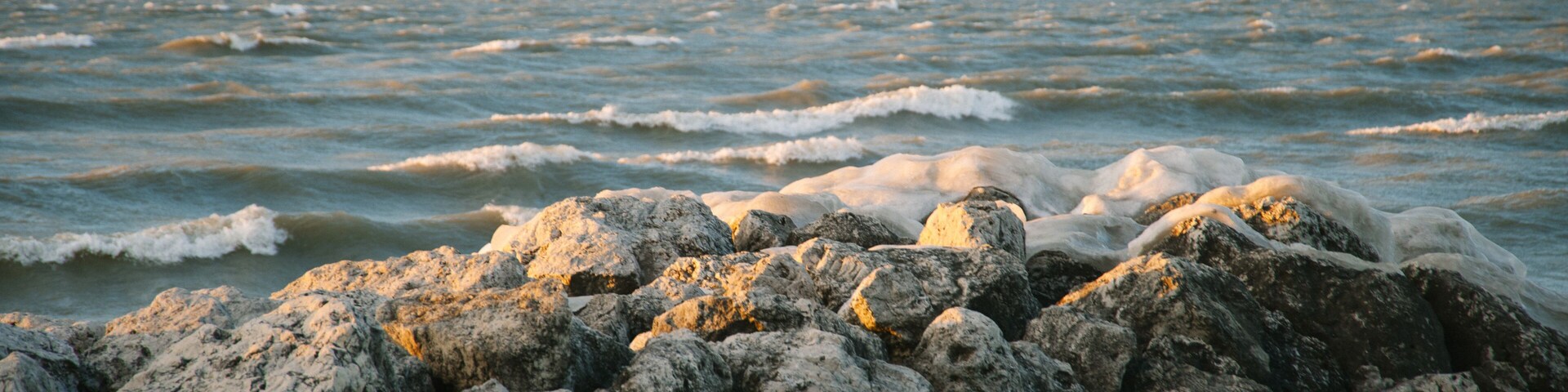 A rocky shoreline with waves crashing against the rocks under a clear sky.