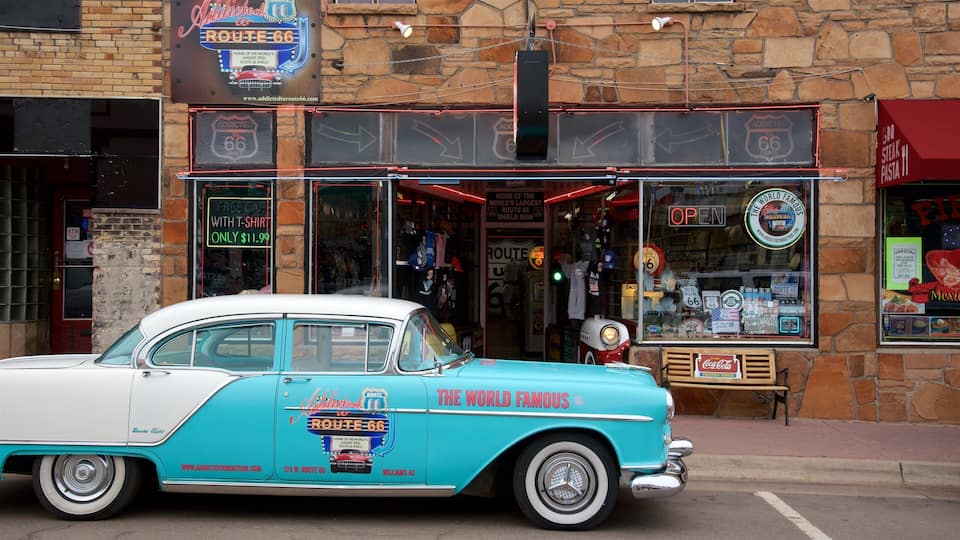 A turquoise and white vintage car parked in front of a Route 66-themed shop with neon signs and merchandise.