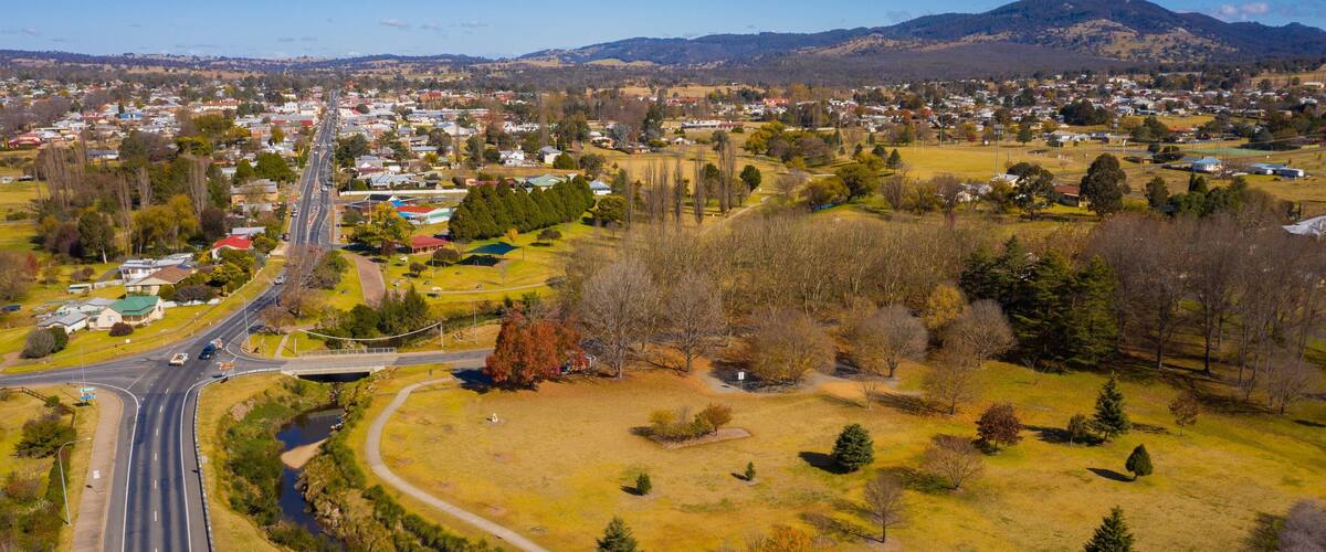 An aerial view of a town with a main road, a bridge, and surrounding fields and trees.