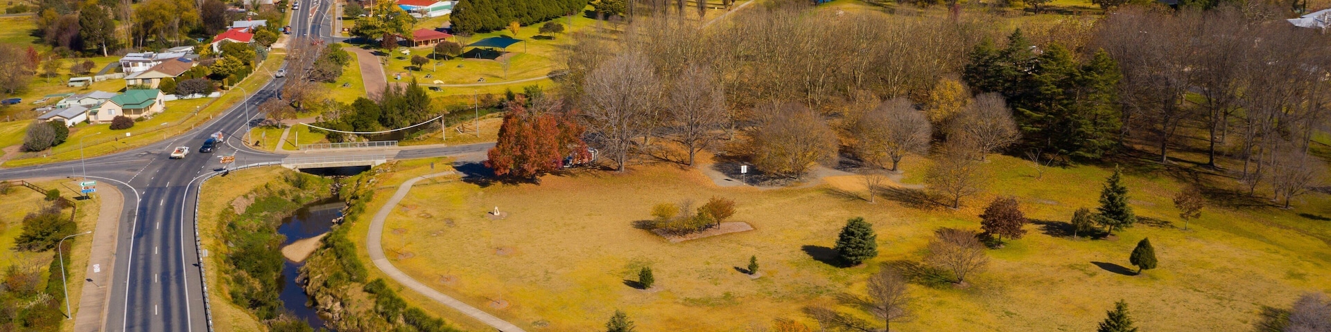 An aerial view of a town with a main road, a bridge, and surrounding fields and trees.