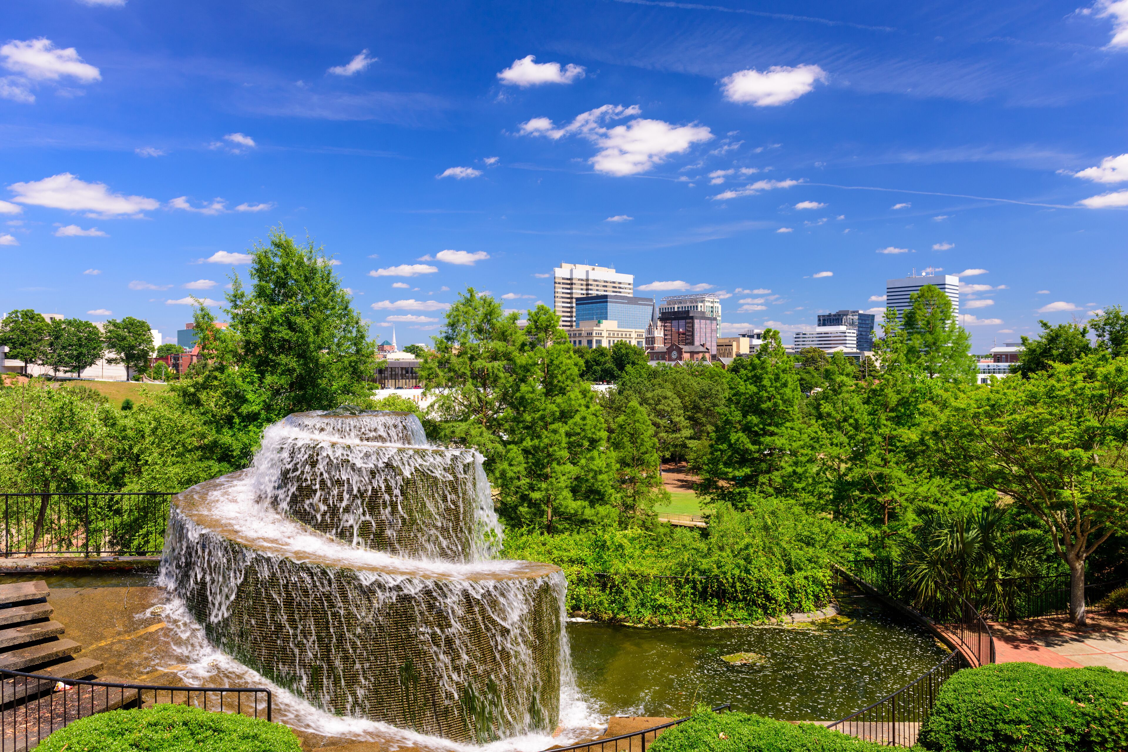 A multi-tiered waterfall in a park with a city skyline in the background.
