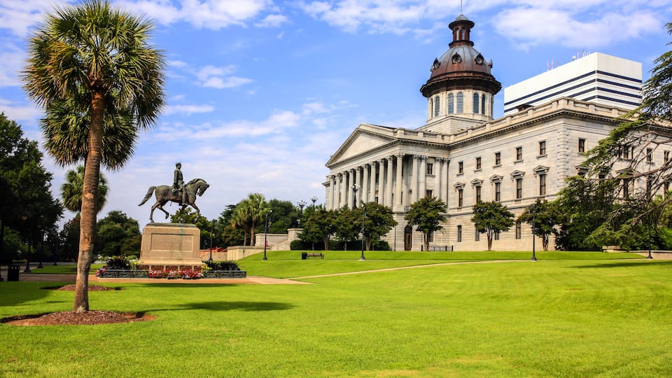 A large building with a dome and columns, surrounded by a well-maintained lawn and a statue of a horse.