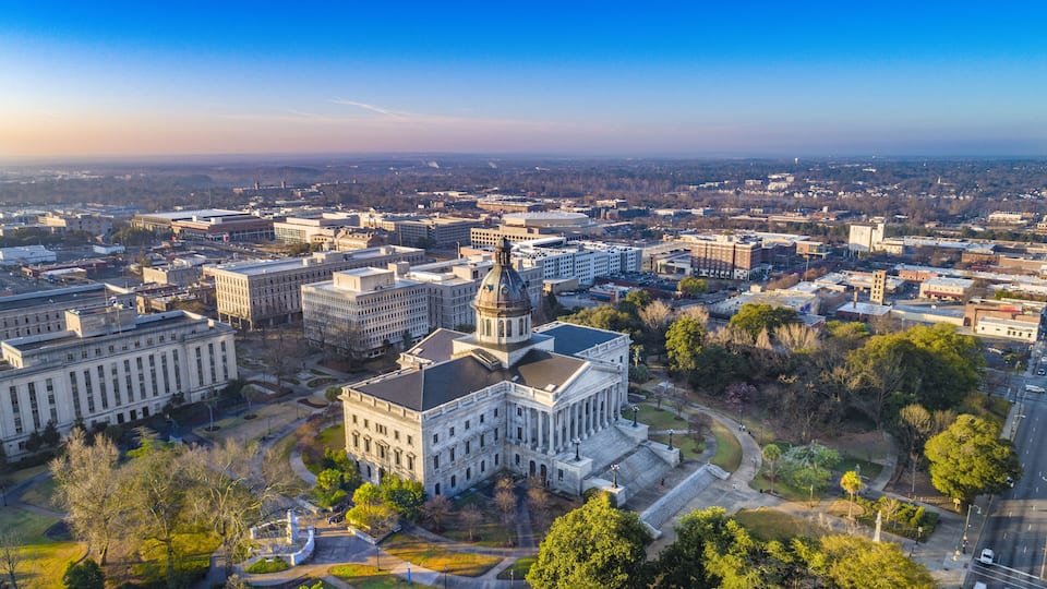 A cityscape with prominent government buildings, including a large white building with columns and a dome, surrounded by smaller structures and greenery.