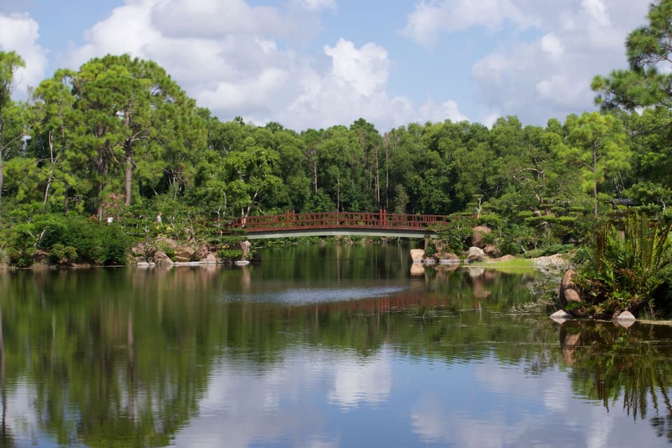 Un lago tranquilo con un puente rojo, rodeado de exuberantes árboles verdes y rocas.
