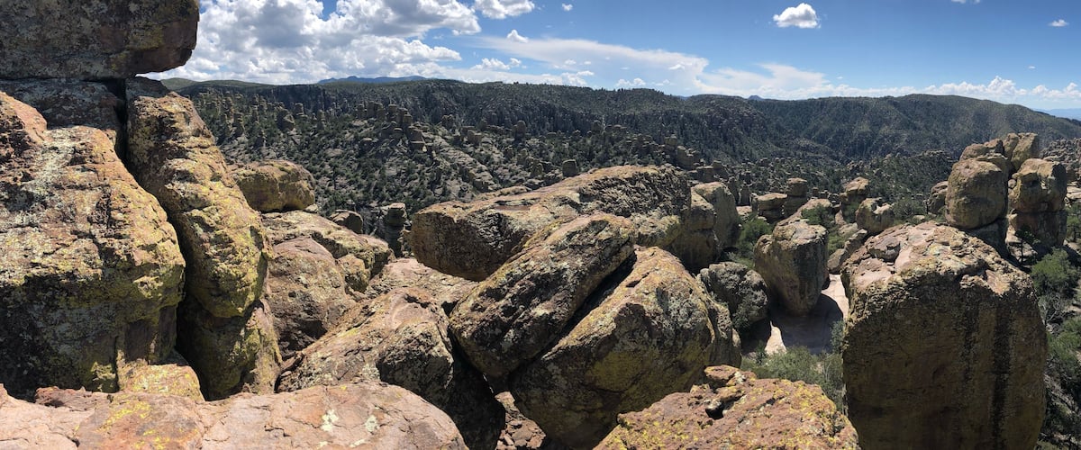 A rocky landscape with prominent boulders and a forested mountain range in the background.