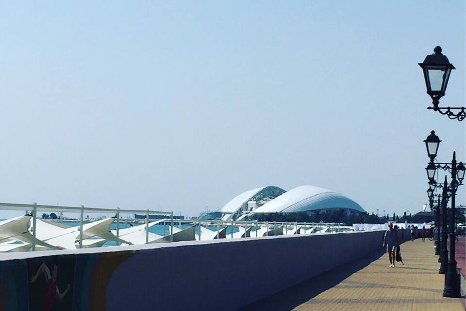 A waterfront promenade with a modern architectural structure, a pedestrian walkway, and a row of street lamps.