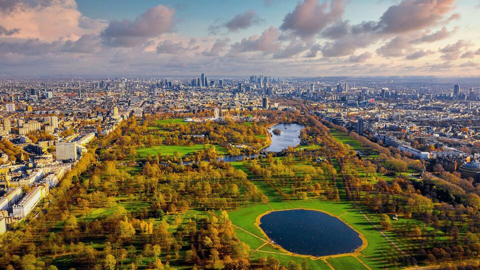An aerial view of a city with a large park, a lake, and surrounding buildings.