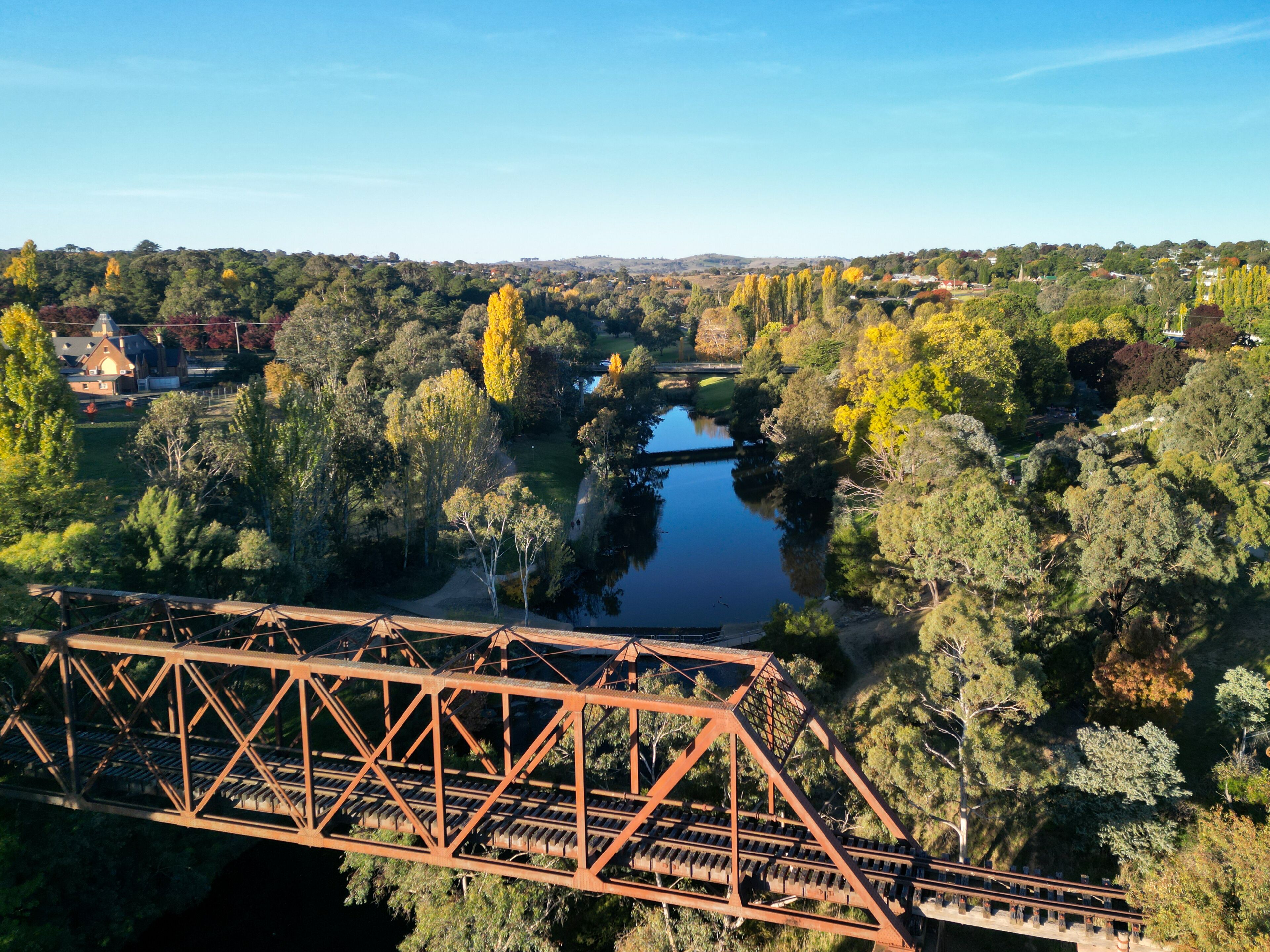 Eine Brücke über einen Fluss, umgeben von Bäumen und einer in der Ferne liegenden Stadt.