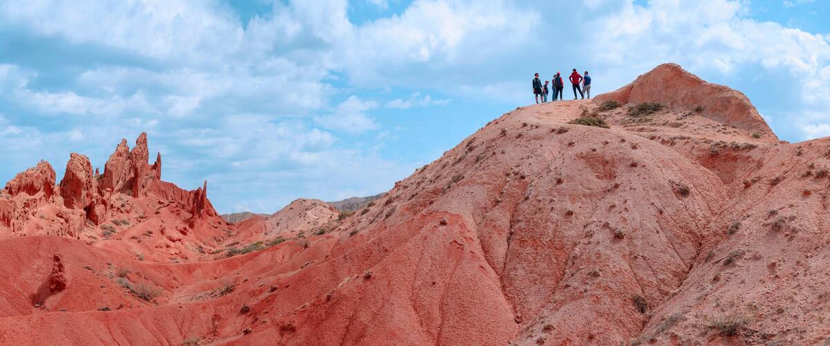 Un grupo de personas sobre una formación rocosa roja, con un cielo despejado al fondo.