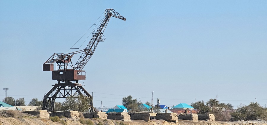 A large mining crane in a rural area with scattered buildings and sparse vegetation.