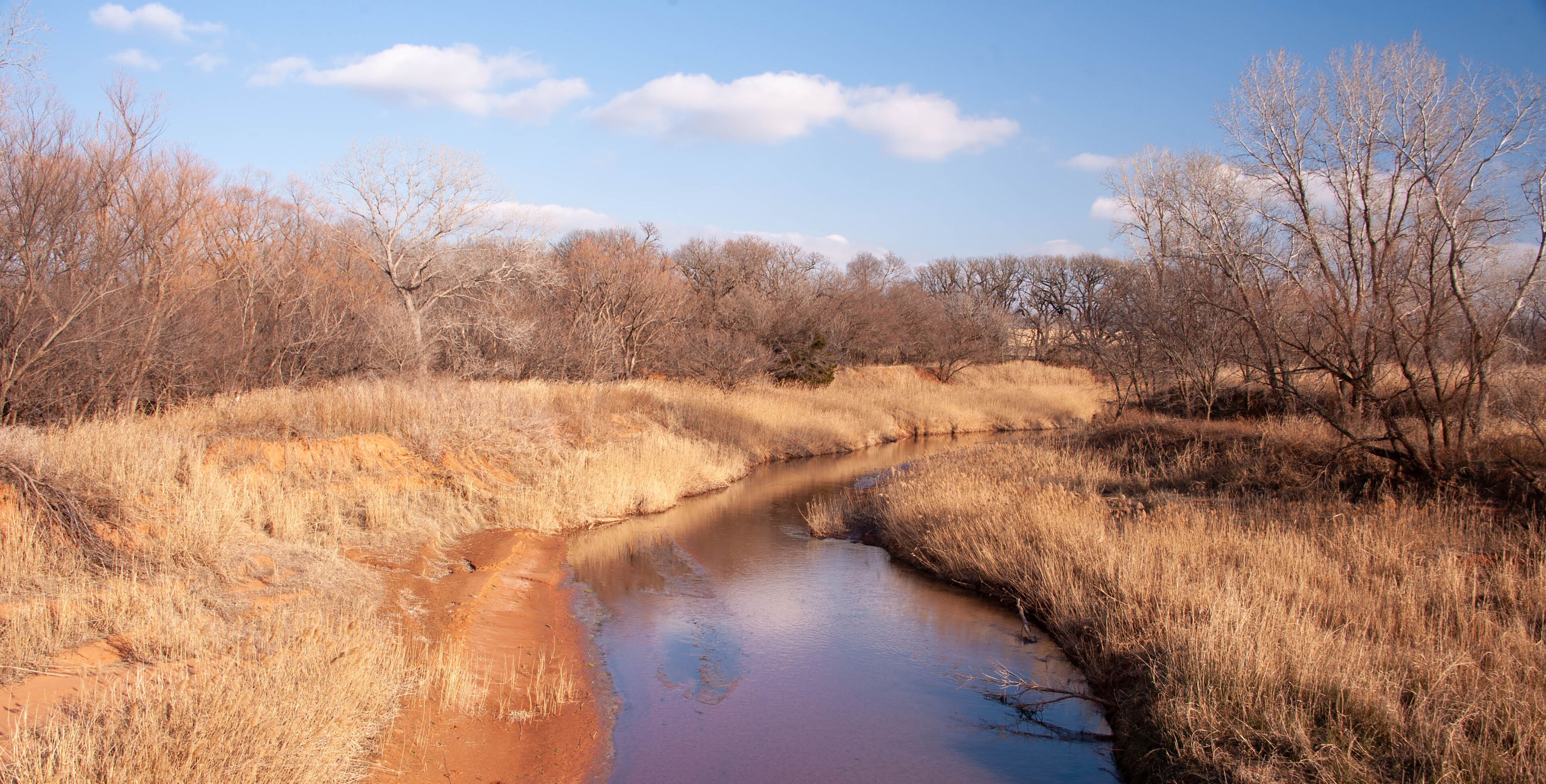 A river meandering through a dry, grassy landscape with sparse trees and a clear sky.