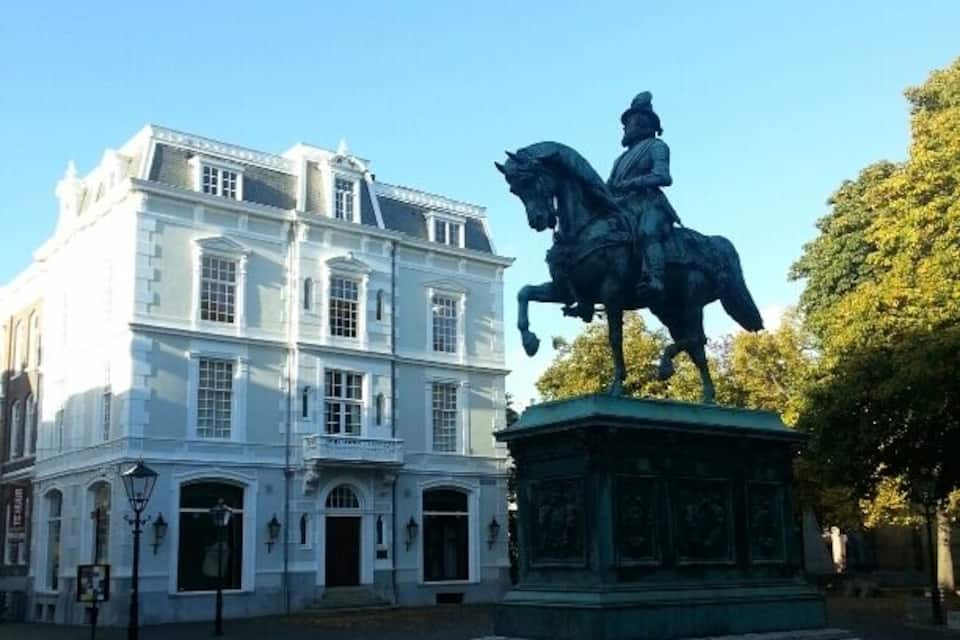 Una estatua de un hombre a caballo frente a un edificio blanco con ventanales de arco.