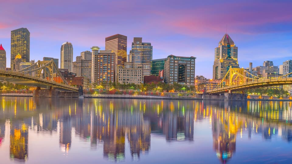A city skyline with high-rise buildings, a river reflecting the city lights, and a bridge spanning the river.