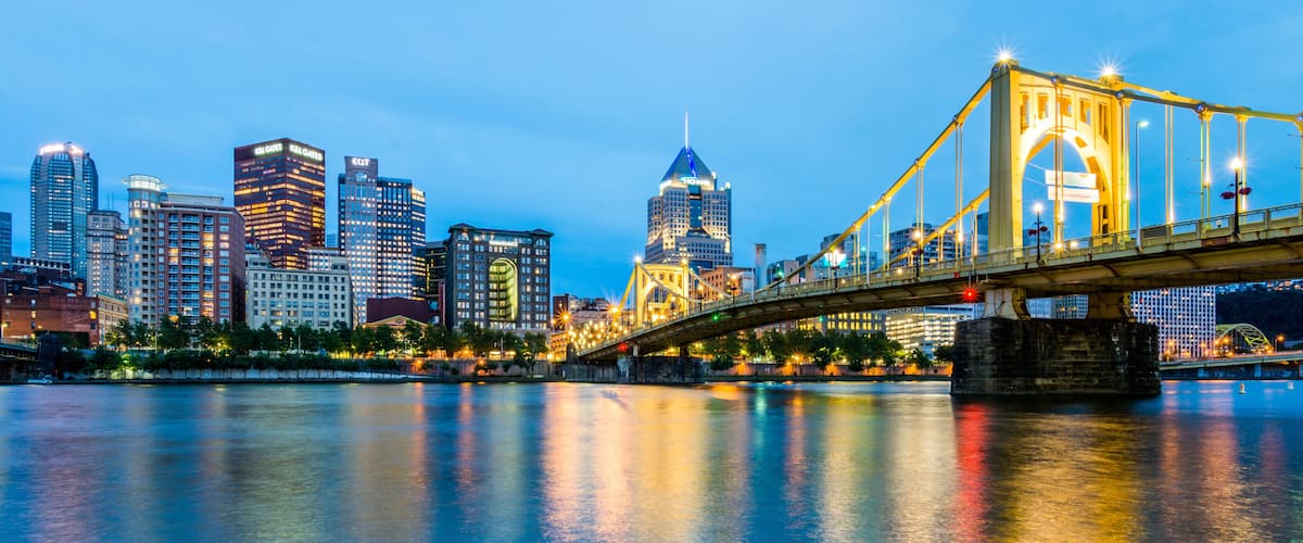 A city skyline with illuminated buildings, a prominent bridge, and a calm river reflecting the lights.