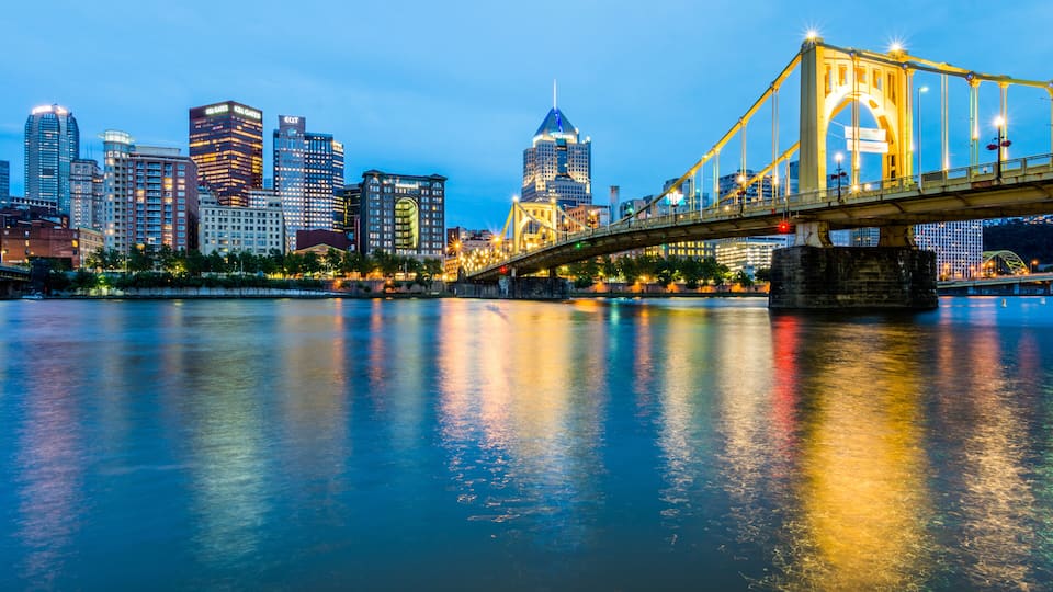 A city skyline with illuminated buildings, a prominent bridge, and a calm river reflecting the lights.