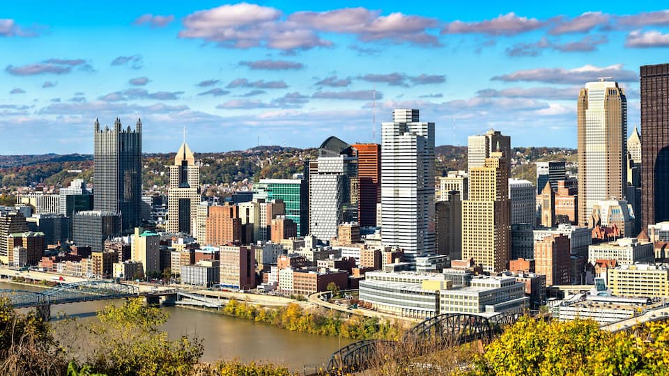 A city skyline with a river in the foreground and hills in the background.
