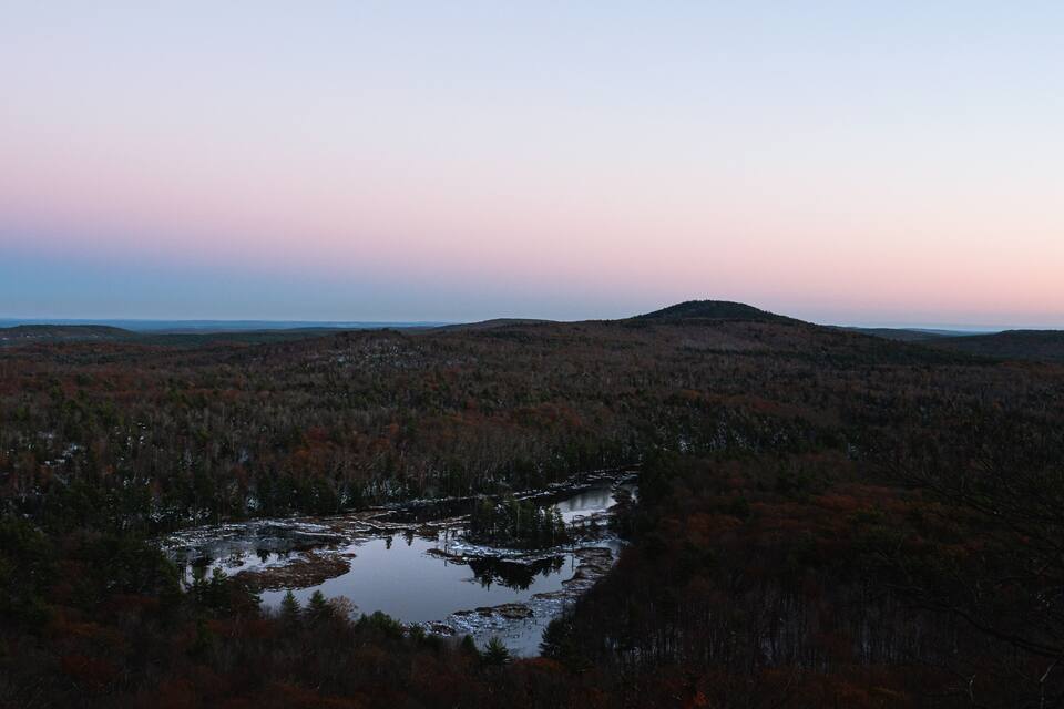 A landscape with a river, forested hills, and a distant mountain range.