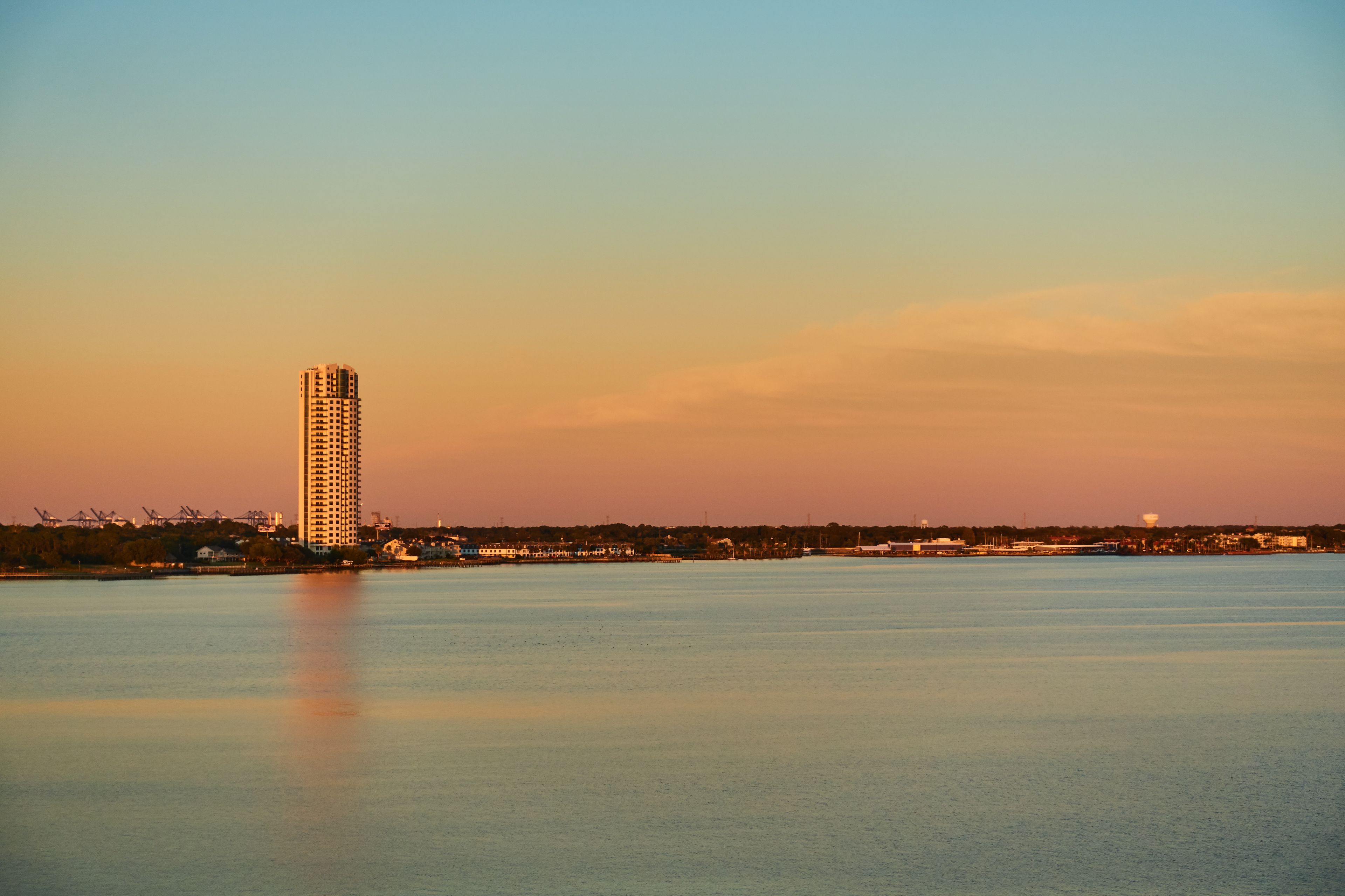A calm body of water with a tall building and a distant shoreline.