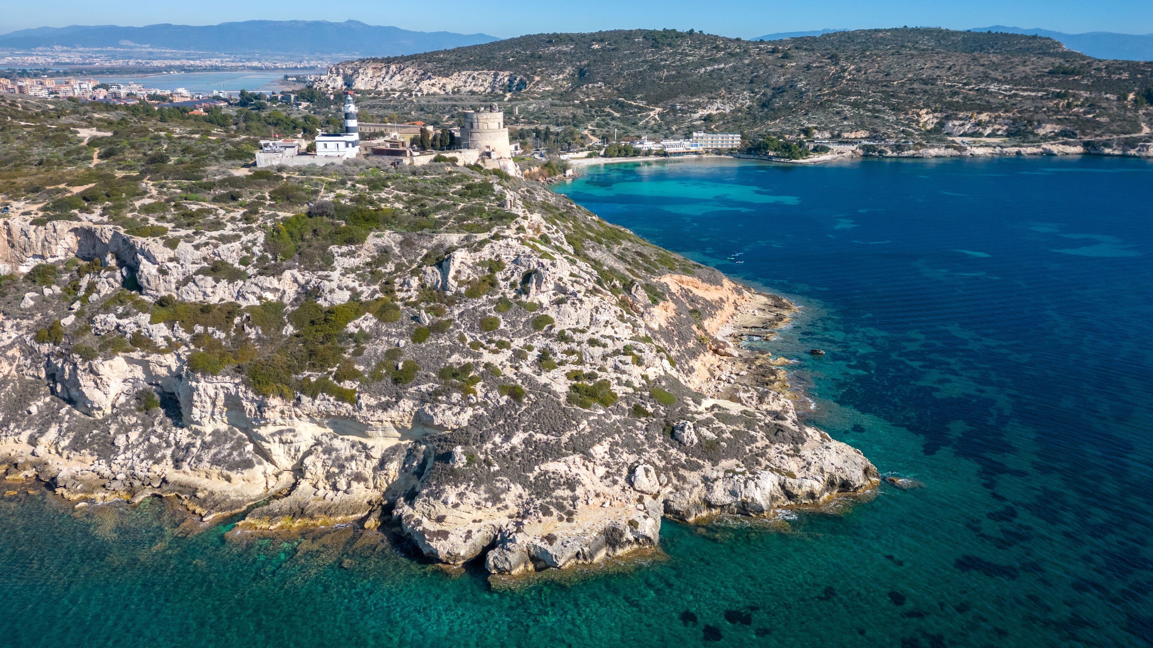 Aerial view with drone of the Sella del Diavolo in Cagliari. Sunny day, crystal clear sea with boats.